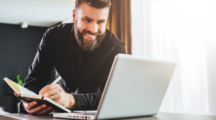 bearded man smiling and reading something on laptop