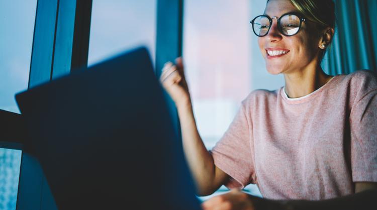 woman wearing glasses smiling looking at laptop screen