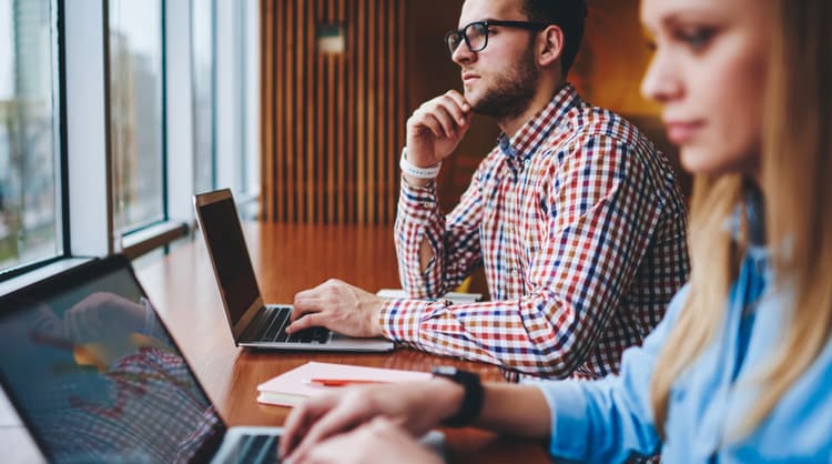 man working on laptop alongside woman colleague