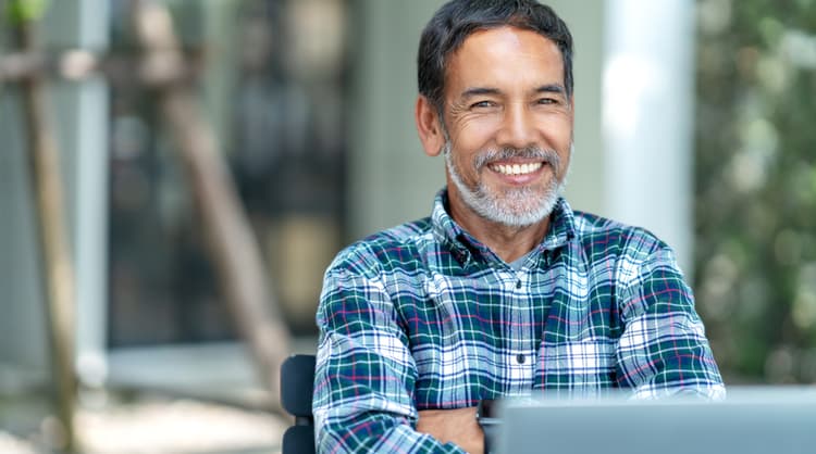 older asian man smiling at camera with laptop