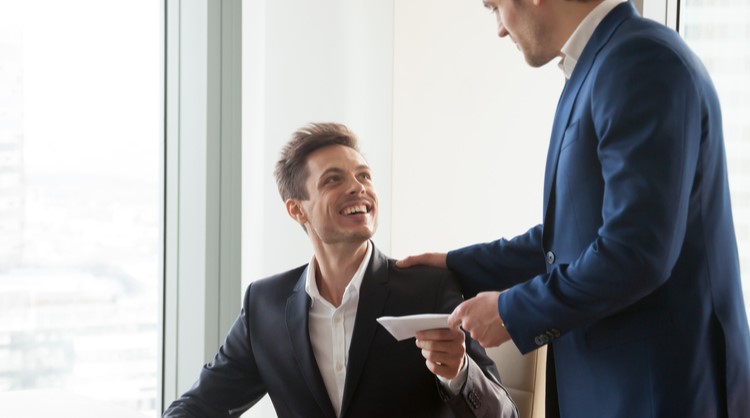 male boss giving envelope to male employee