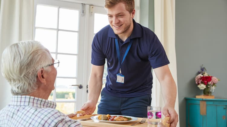 male aged care worker serving food to elderly man