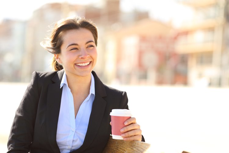 woman in business attire smiling with coffee in hand