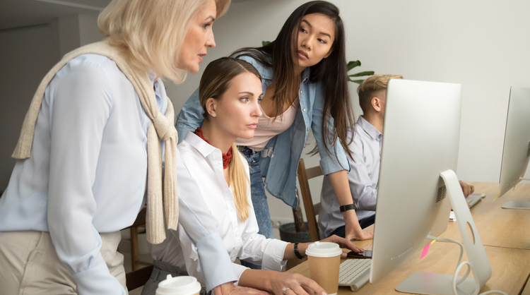 multiracial colleagues talking as a team around assistant's computer