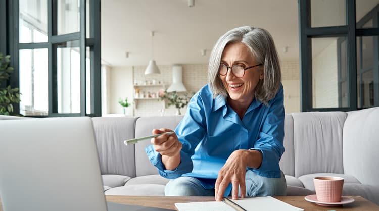 older woman using laptop and taking notes