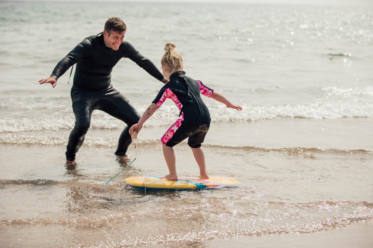 male surfing instructor teaching little girl how to surf