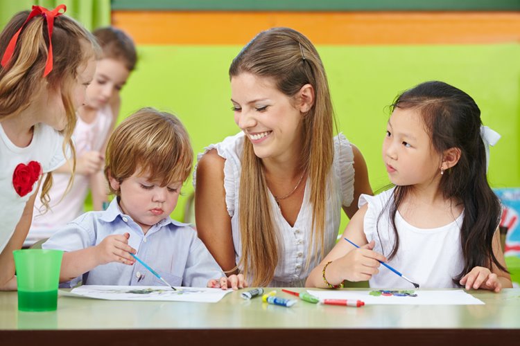 early childhood teacher overseeing paintings from children