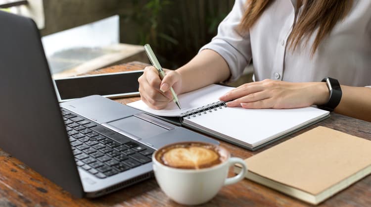 woman studying online taking notes on book