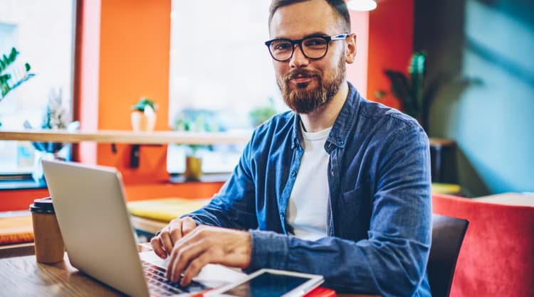 man working on laptop facing camera and smiling