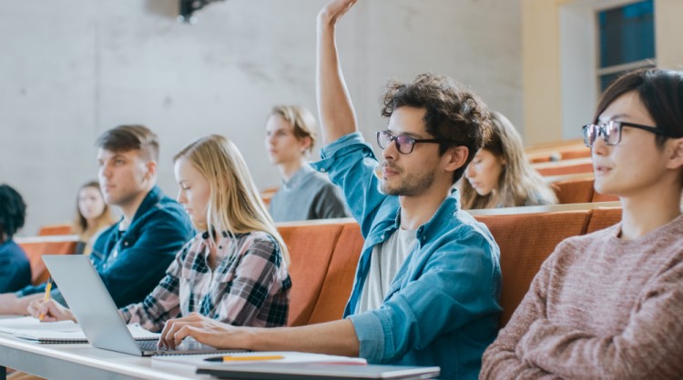 male student putting hand up in lecture room