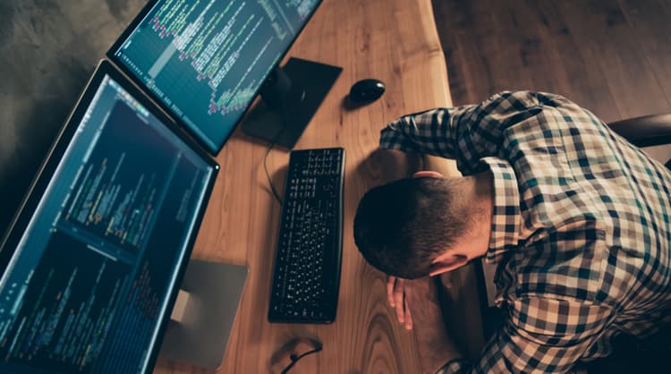 man overwhelmed at computer task, facing three computer monitors