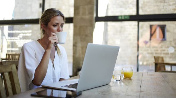 young woman sipping coffee while working on laptop