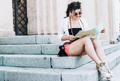 young woman with sunglasses sitting on step and looking at map